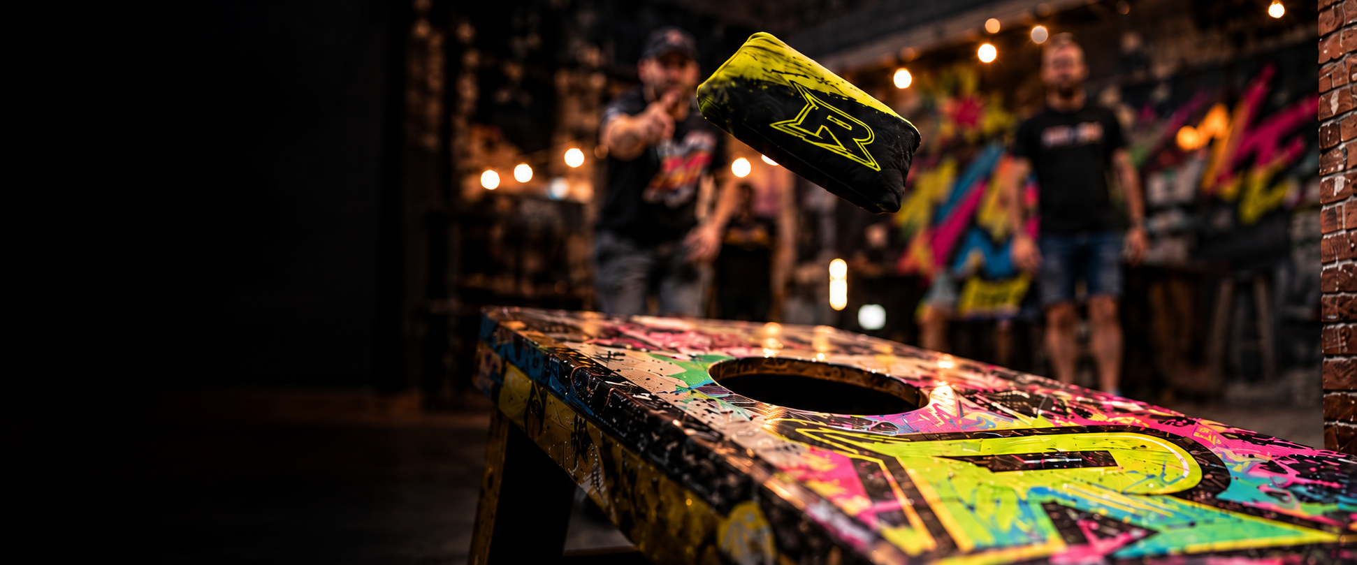 A Redline bag flying toward a graffiti cornhole board on league night